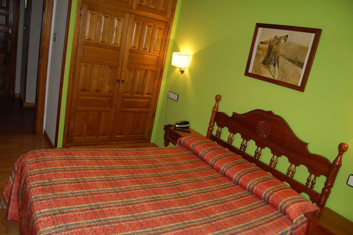 Une pièce avec un lit en bois, un mur vert et un tableau encadré.