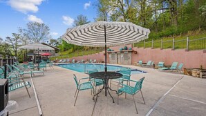 A pool area with lounge chairs, a table, and an umbrella. - Country Town N'Suites (Gatlinburg)
