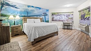 A bedroom with a large bed, a desk, and a chair, a window with a waterfall view, and a mural of a forest scene. - Country Town N'Suites (Gatlinburg)