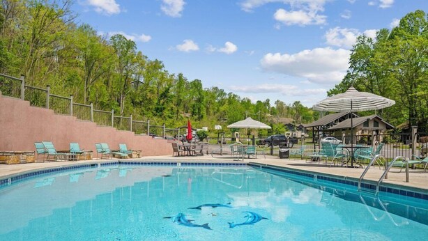 A swimming pool with clear blue water, surrounded by lounge chairs and umbrellas. - Country Town N'Suites (Gatlinburg)