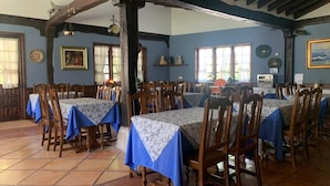A dining area with multiple tables and chairs, wooden beams on the ceiling, and a tiled floor. - Hotel Siglo XVIII (Santillana del Mar)