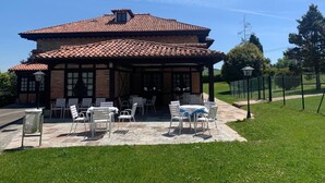 A two-story building with a tiled roof, a covered patio area with outdoor seating, and a brick facade. - Hotel Siglo XVIII (Santillana del Mar)