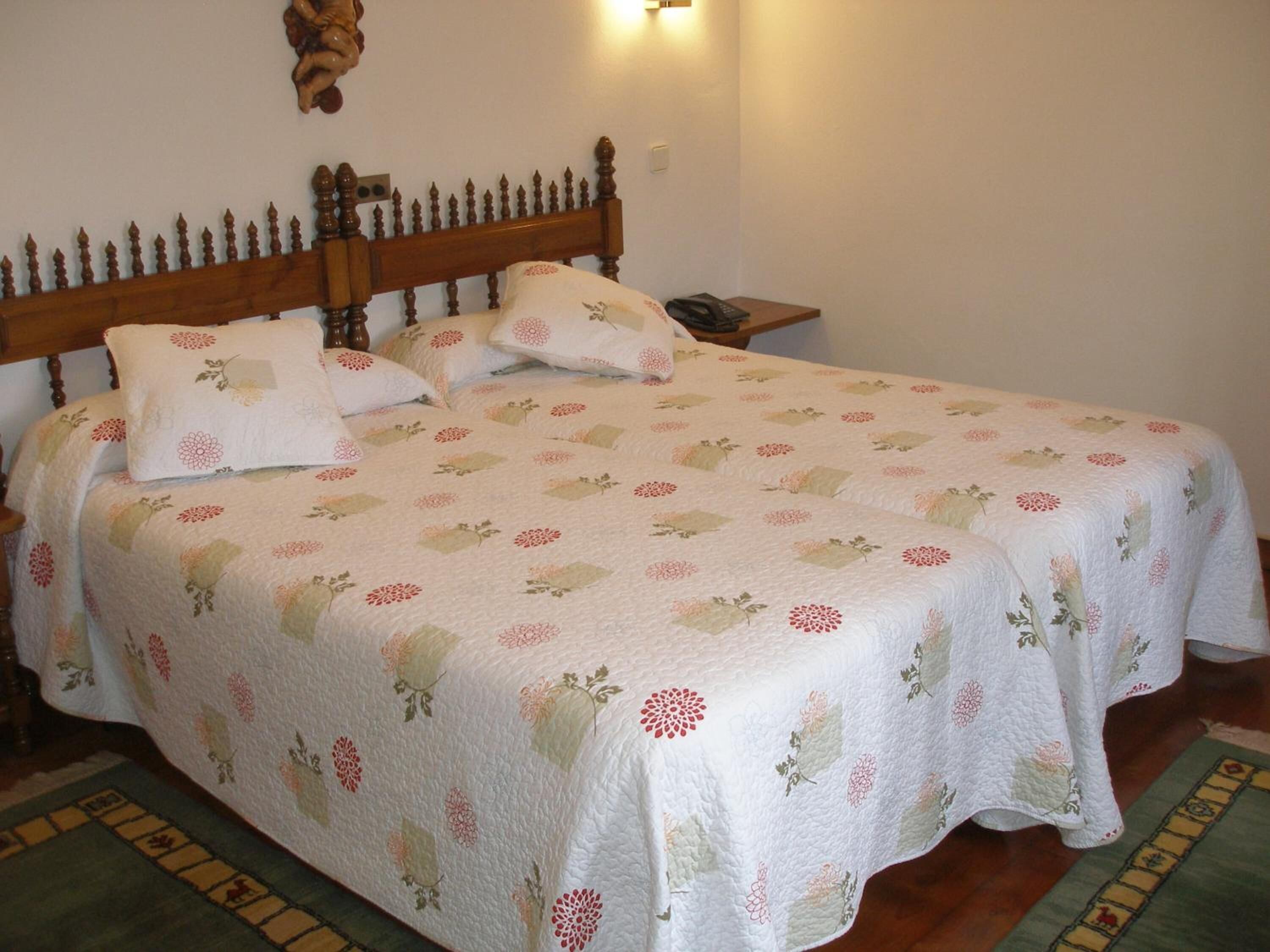 A neatly made bed with floral bedding, a wooden headboard, and a nightstand with a lamp.