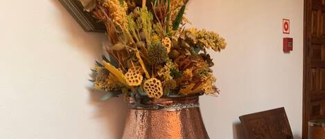 A copper vase with dried flowers on a wooden cabinet in a room with a mirror and a framed painting on the wall.