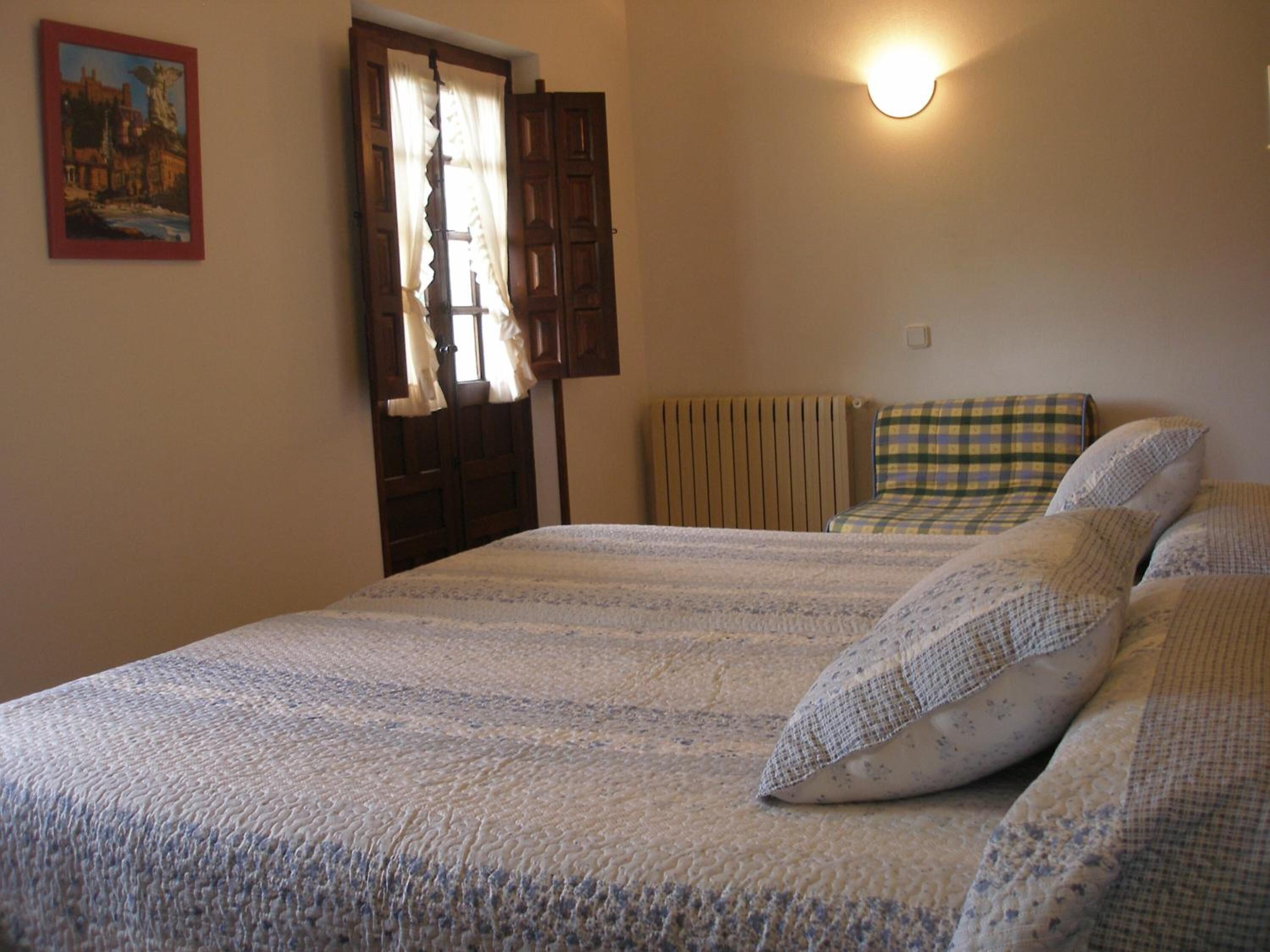 Une chambre à coucher avec un lit, un radiateur, une fenêtre avec des rideaux et une lampe fixée au mur.