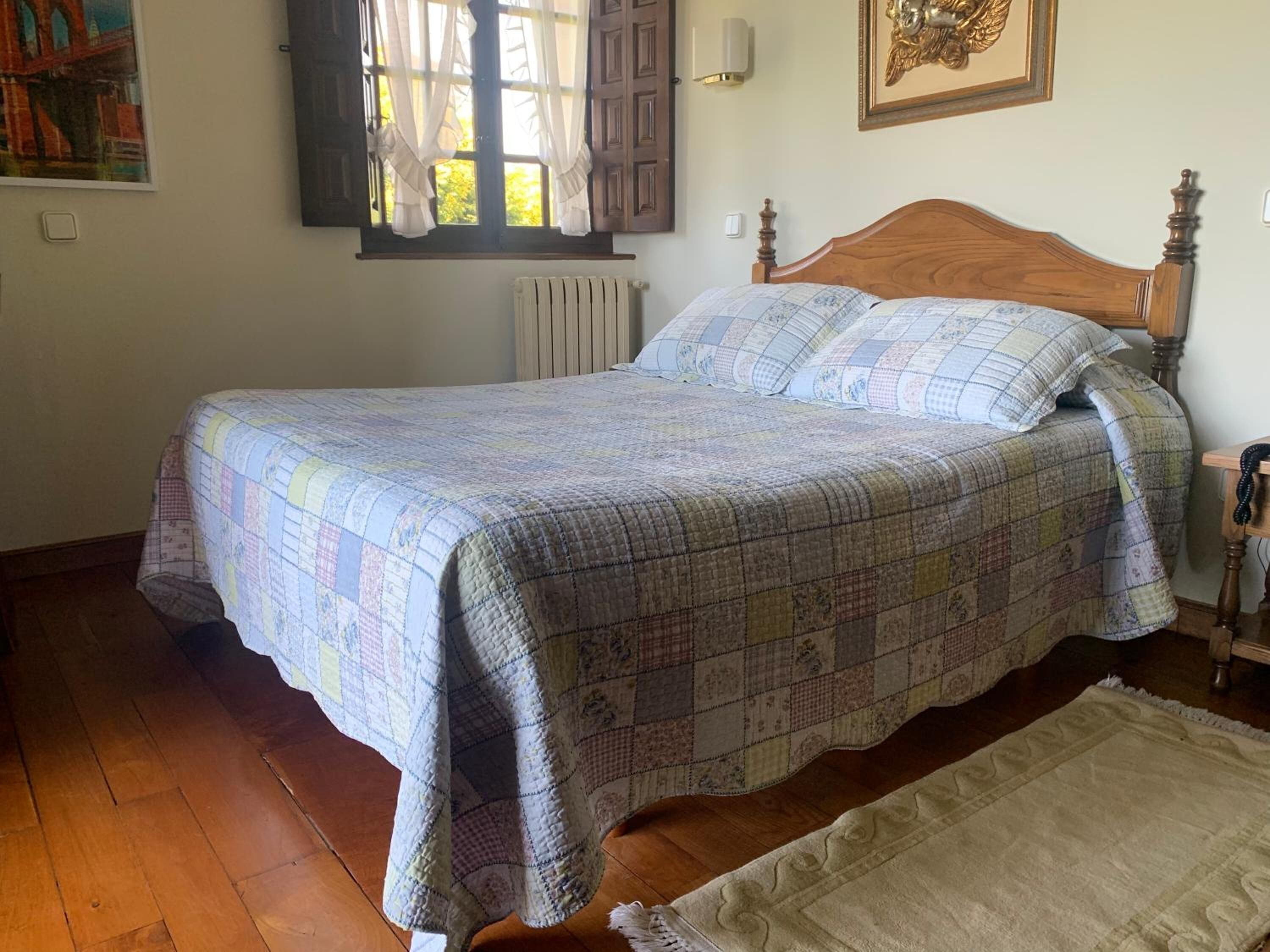 A bedroom with a wooden bed, a window with curtains, a radiator, and a framed picture on the wall.
