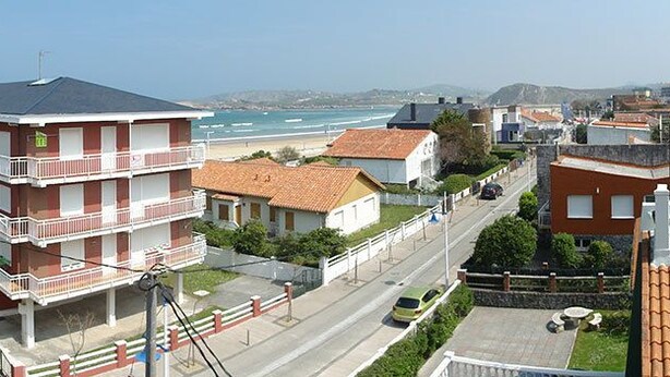 A coastal residential area with multi-story buildings, a beach view, and a clear sky. - Vivero Playa (Suances)