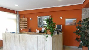A reception area with a wooden reception desk, a bulletin board, a potted plant, a computer, and a framed picture on the wall. - Vivero Playa (Suances)