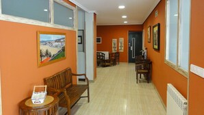 A hallway with orange walls, wooden benches, a small table with a basket, and framed pictures on the walls. - Vivero Playa (Suances)