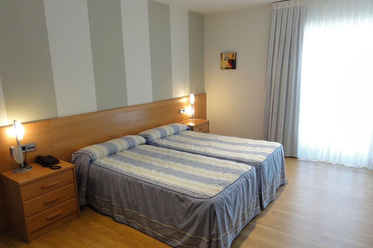 A hotel room with two beds, a wooden headboard, bedside lamps, a telephone, and a small painting on the wall.