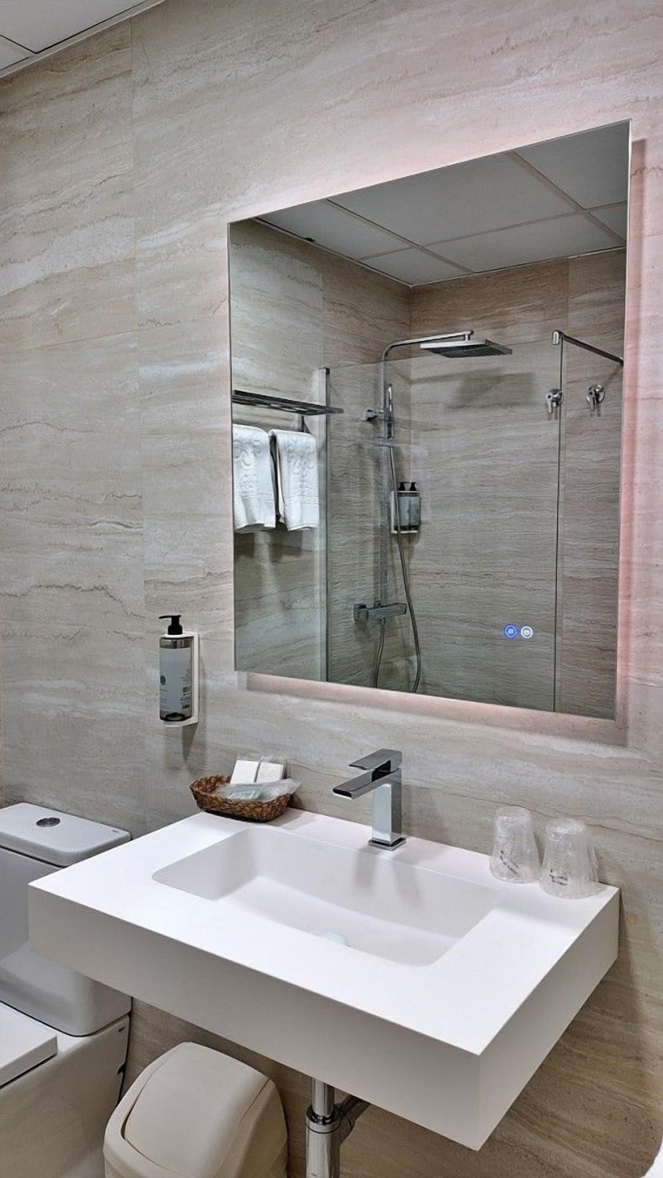 A modern bathroom with a large mirror, a white sink, and a glass-enclosed shower.