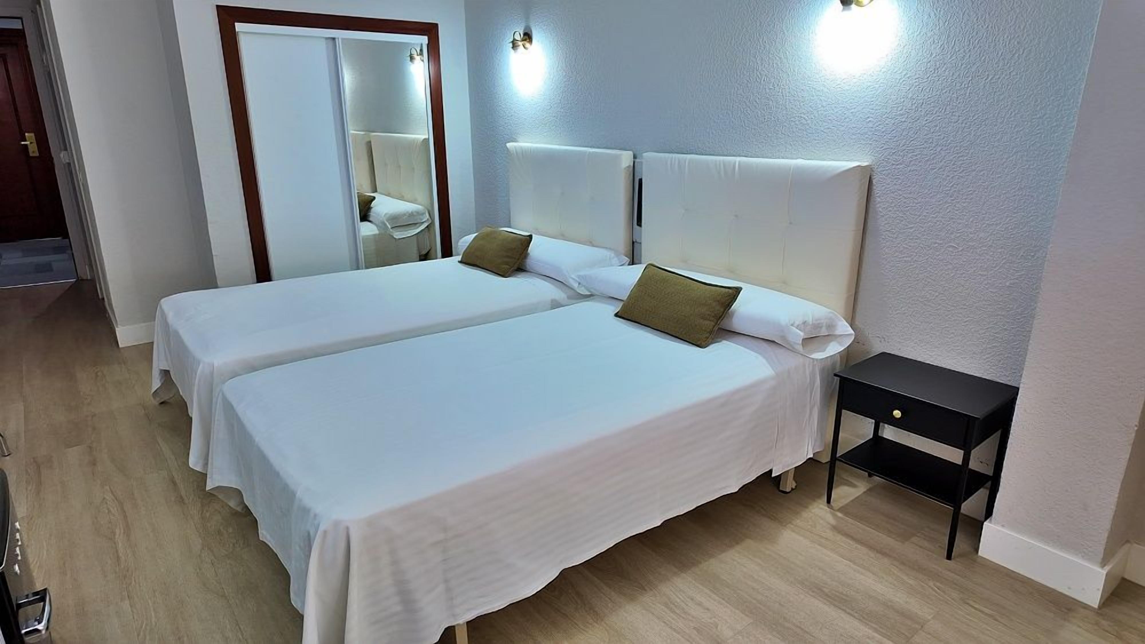 Ett hotellrum med två sängar, ett litet sängbord och en spegel.