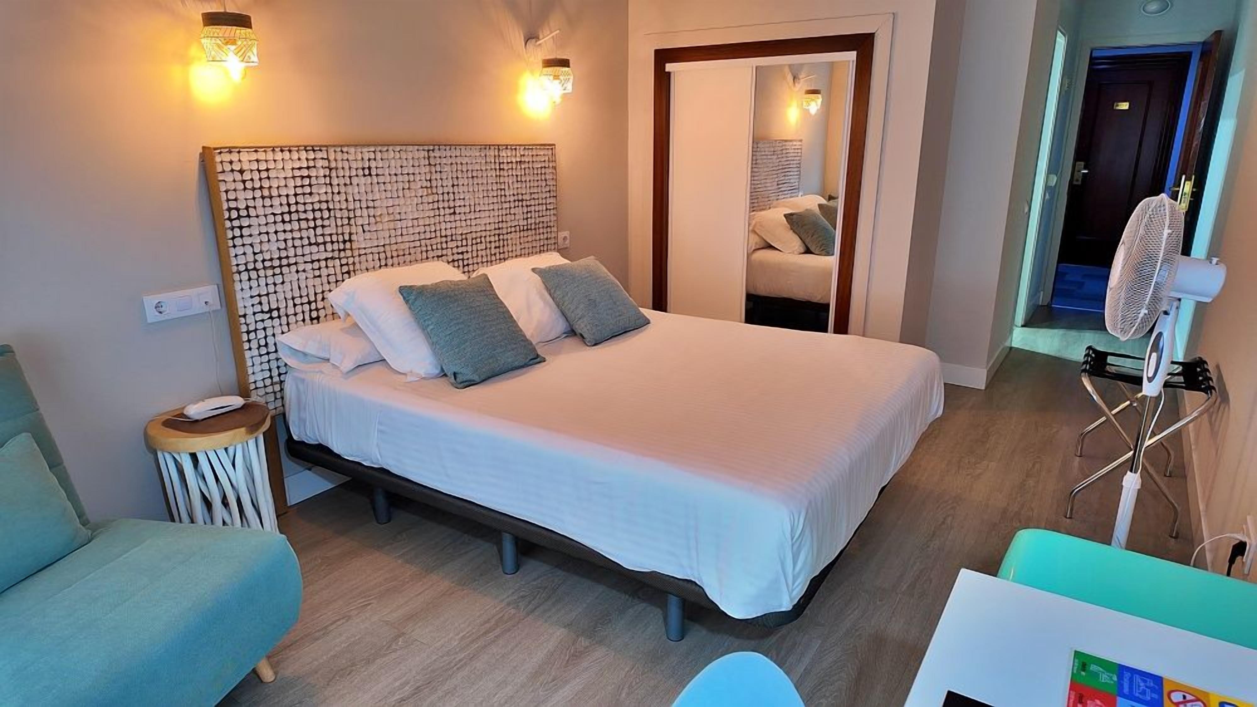 Un dormitorio con cama, mesita de noche, lámpara y espejo.