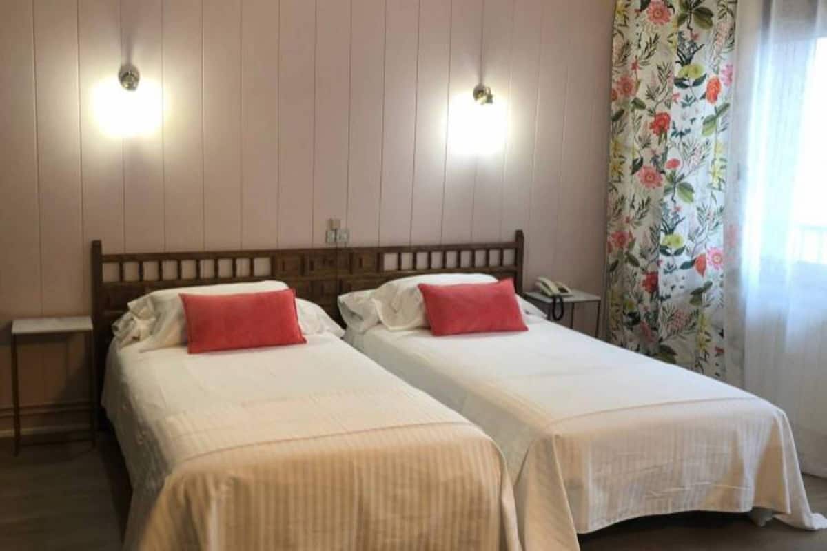 Une chambre double avec deux lits, chacun doté d’un oreiller rouge, d’une tête de lit en bois et d’une petite table de chevet.