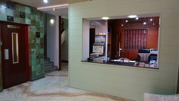 A hotel lobby with a marble floor, a reception desk, and a staircase.