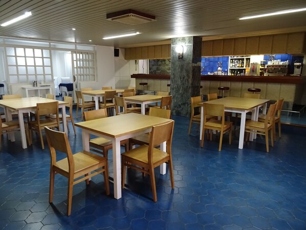 Un comedor con azulejos azules hexagonales, mesas y sillas de madera, un pilar de mármol y una zona de bar con estantes llenos de botellas.
