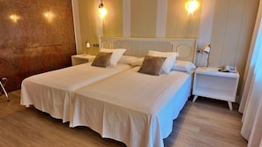 Un letto matrimoniale con biancheria da letto bianca e due cuscini, un comodino con una lampada e un punto luce a parete.