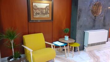 A yellow armchair, a small round table with a potted plant, a framed picture on the wall, and a radiator.