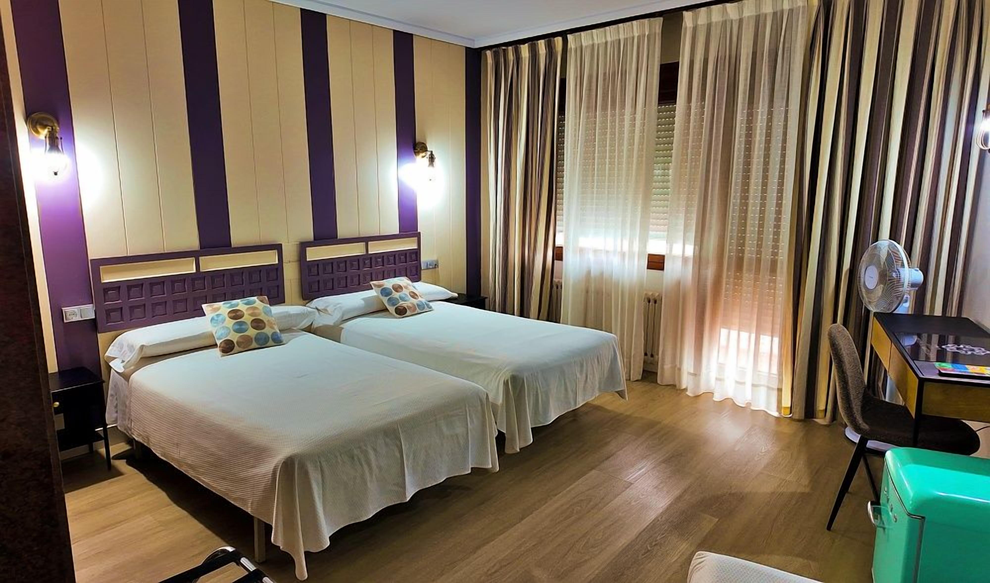 A hotel room with two beds, a desk, a chair, and a window with curtains.