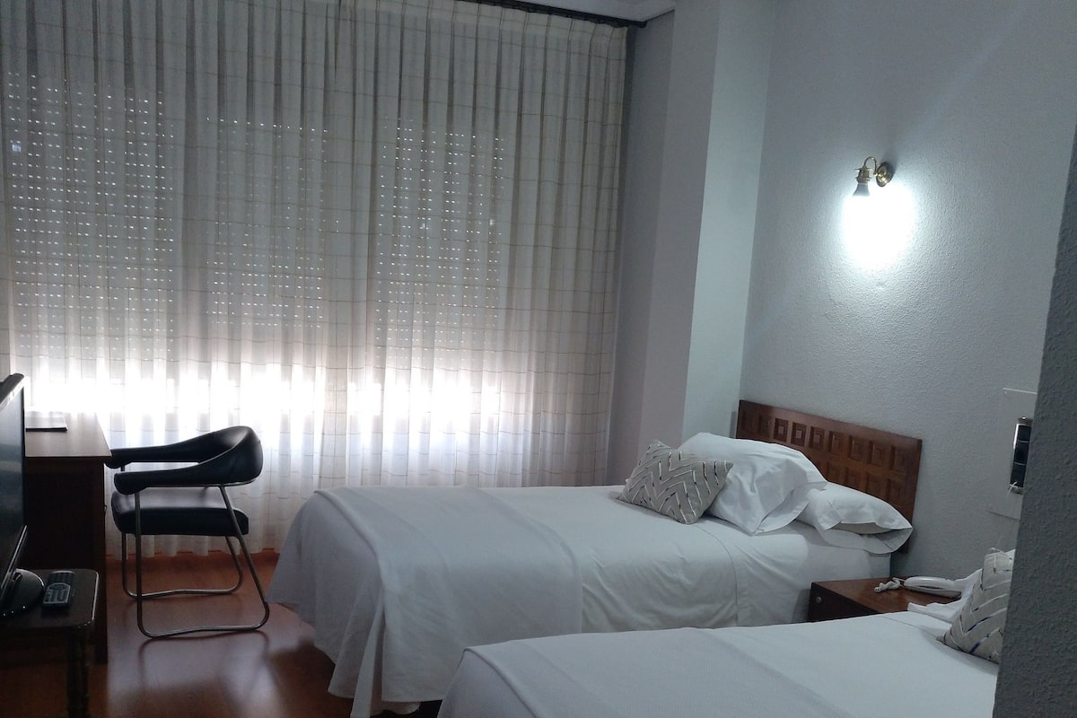 Une chambre d’hôtel avec deux lits, un bureau, une chaise et une fenêtre avec des rideaux.