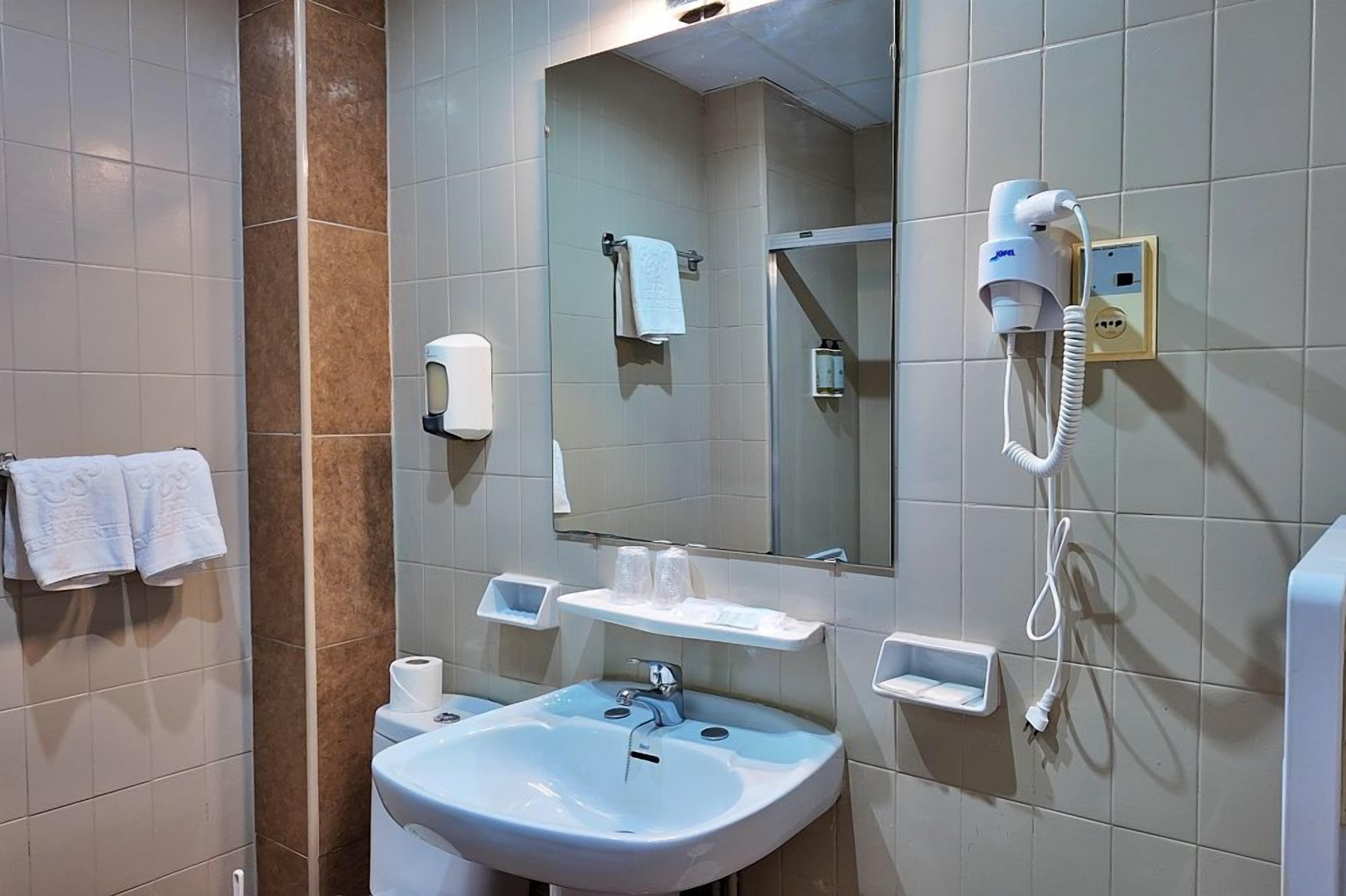 A bathroom with a sink, mirror, towel rack, and a hairdryer on the wall.