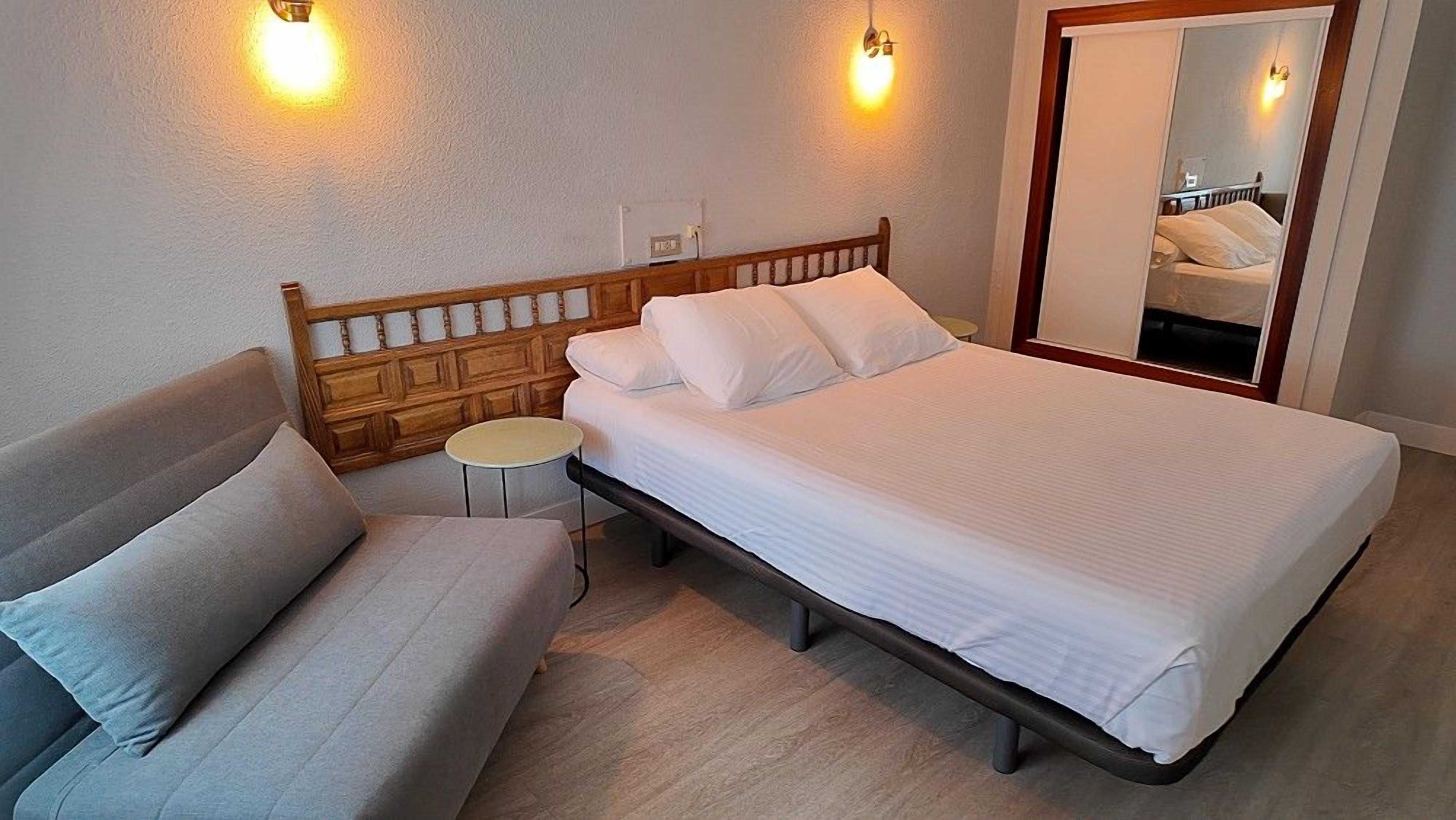 Un dormitori amb un llit, una taula de nit, una cadira i dues làmpades de paret.
