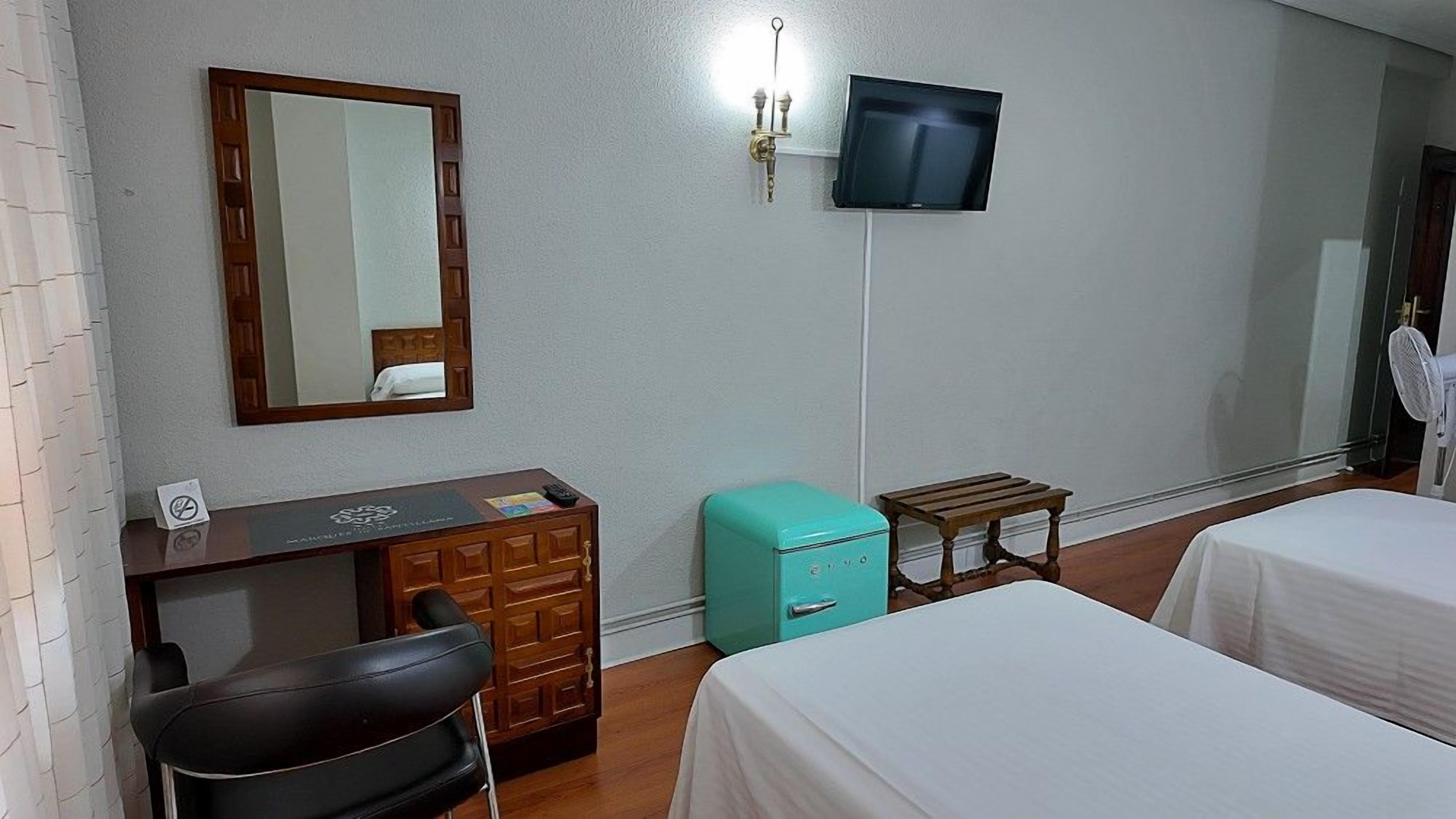 A hotel room with a desk, a television, a small table, and two beds.