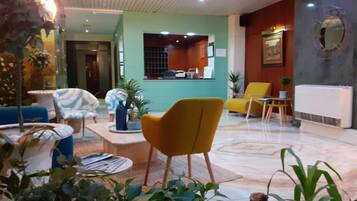 Un hall de hotel con mostrador de recepción, zona de estar con sillas y una mesa de centro.