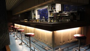 Una zona de bar con mostrador, taburetes y suelo de baldosas.