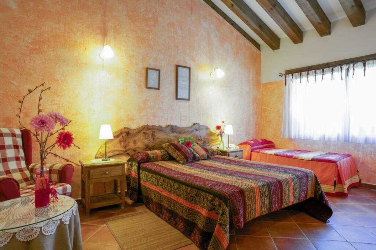 Ein gemütliches Schlafzimmer mit einem großen Bett, zwei Nachttischen, einem kleinen Tisch mit Blumen und einem Fenster mit Vorhängen.