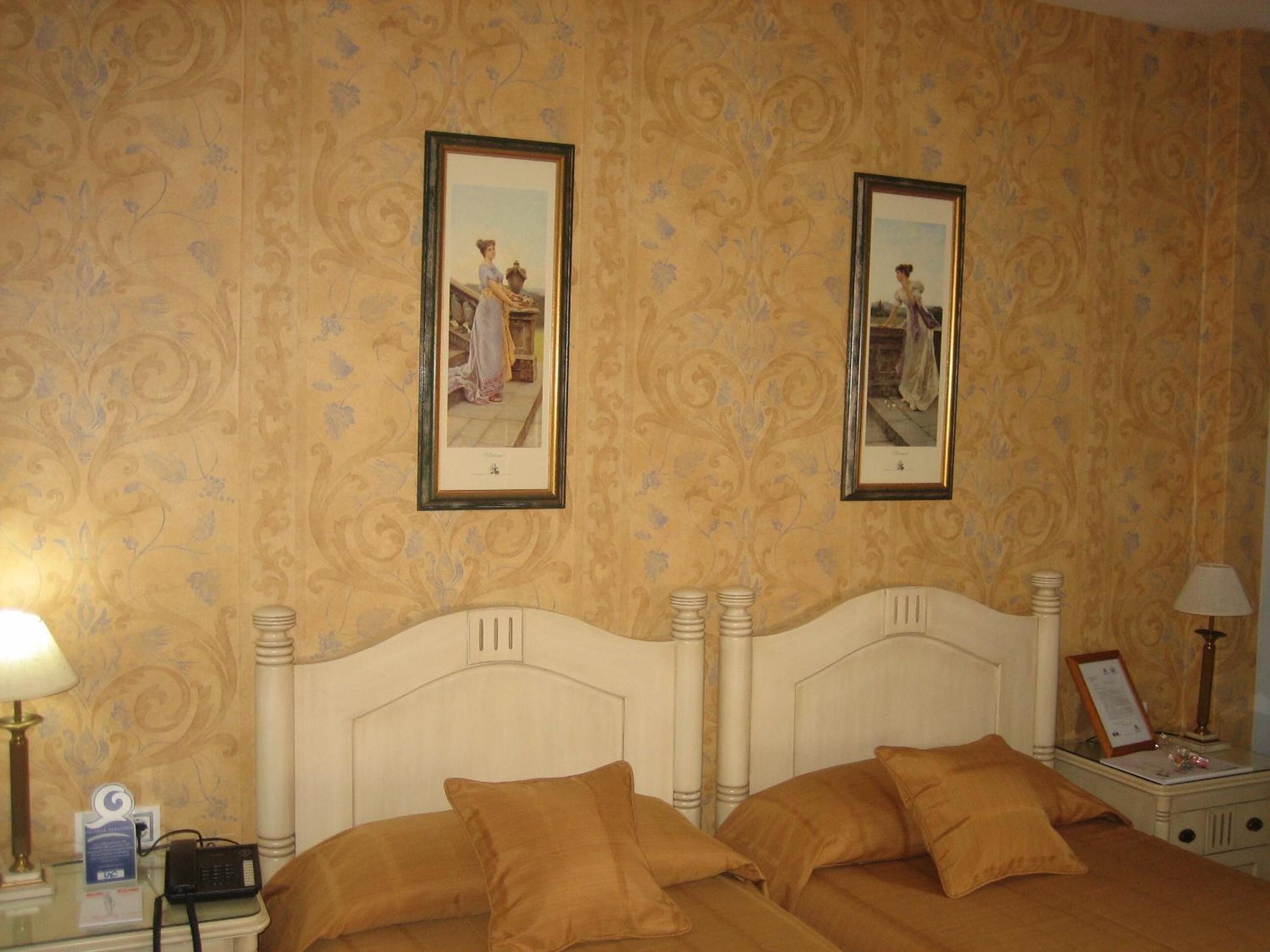 Een hotelkamer met een groot bed, twee ingelijste foto's aan de muur, een nachtkastje met een lamp, en een bijzettafeltje met een lamp.