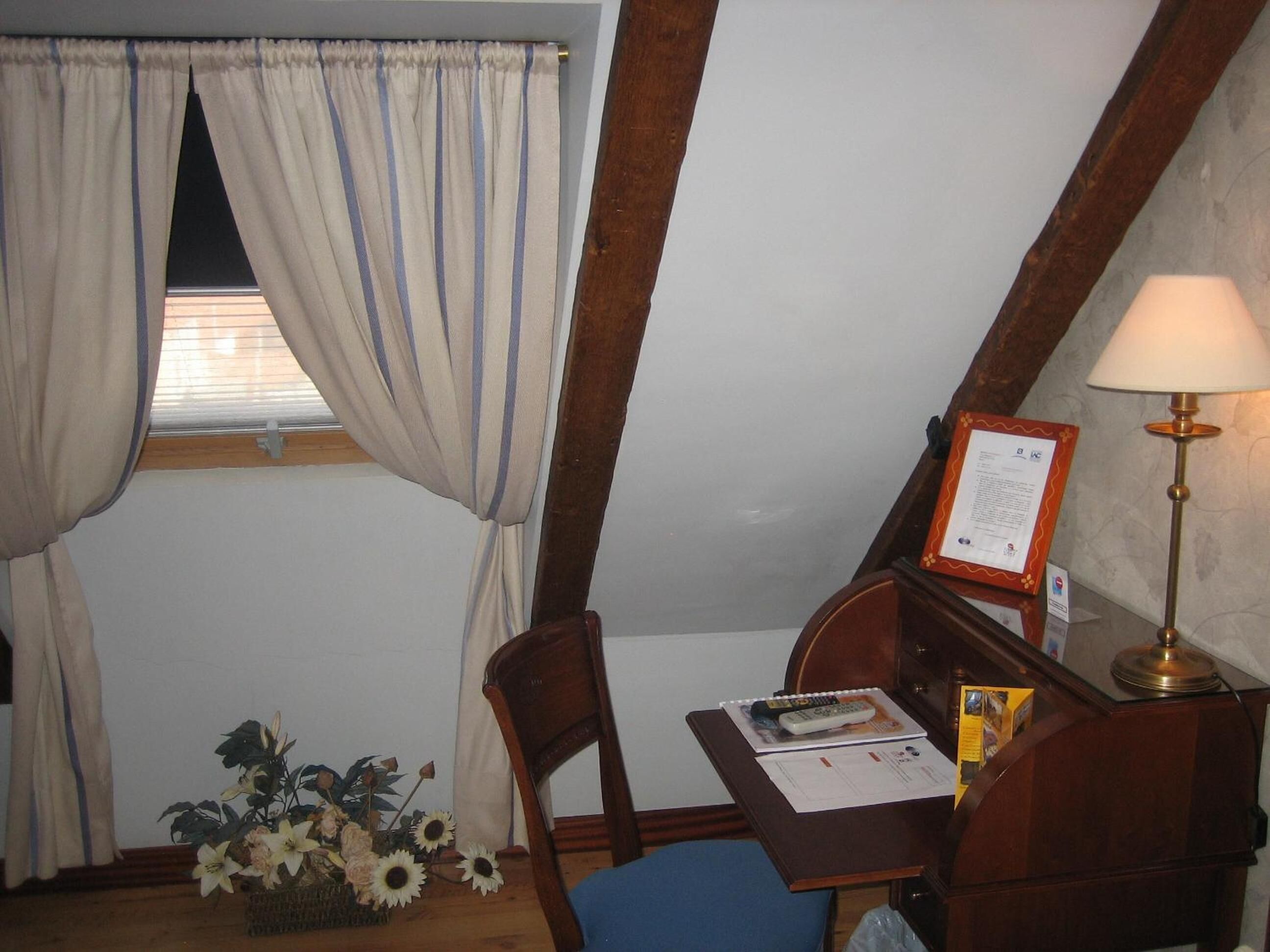 A room with a desk, chair, lamp, and a window with curtains.
