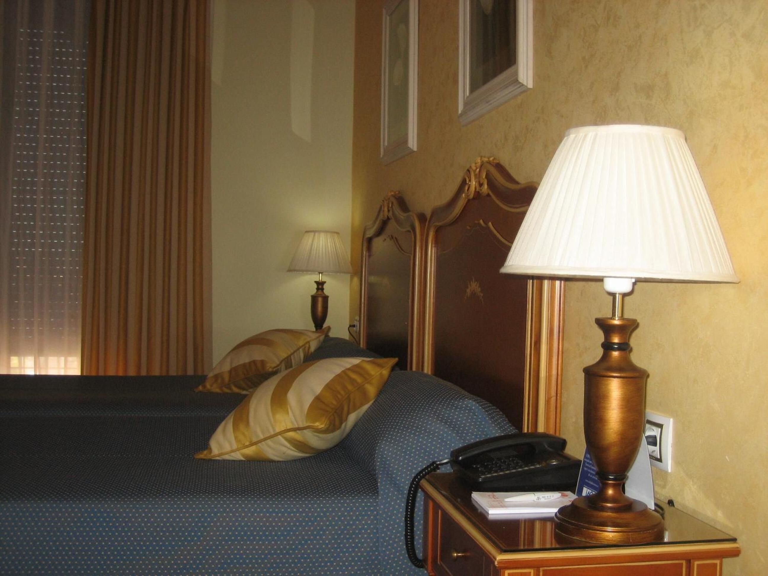 A hotel room with a bed, a nightstand with a lamp, a telephone, and a wall-mounted picture.