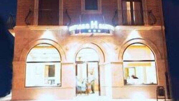 Un hotel de varios pisos con fachada de ladrillo, ventanas iluminadas y un letrero que indica que es un hotel.