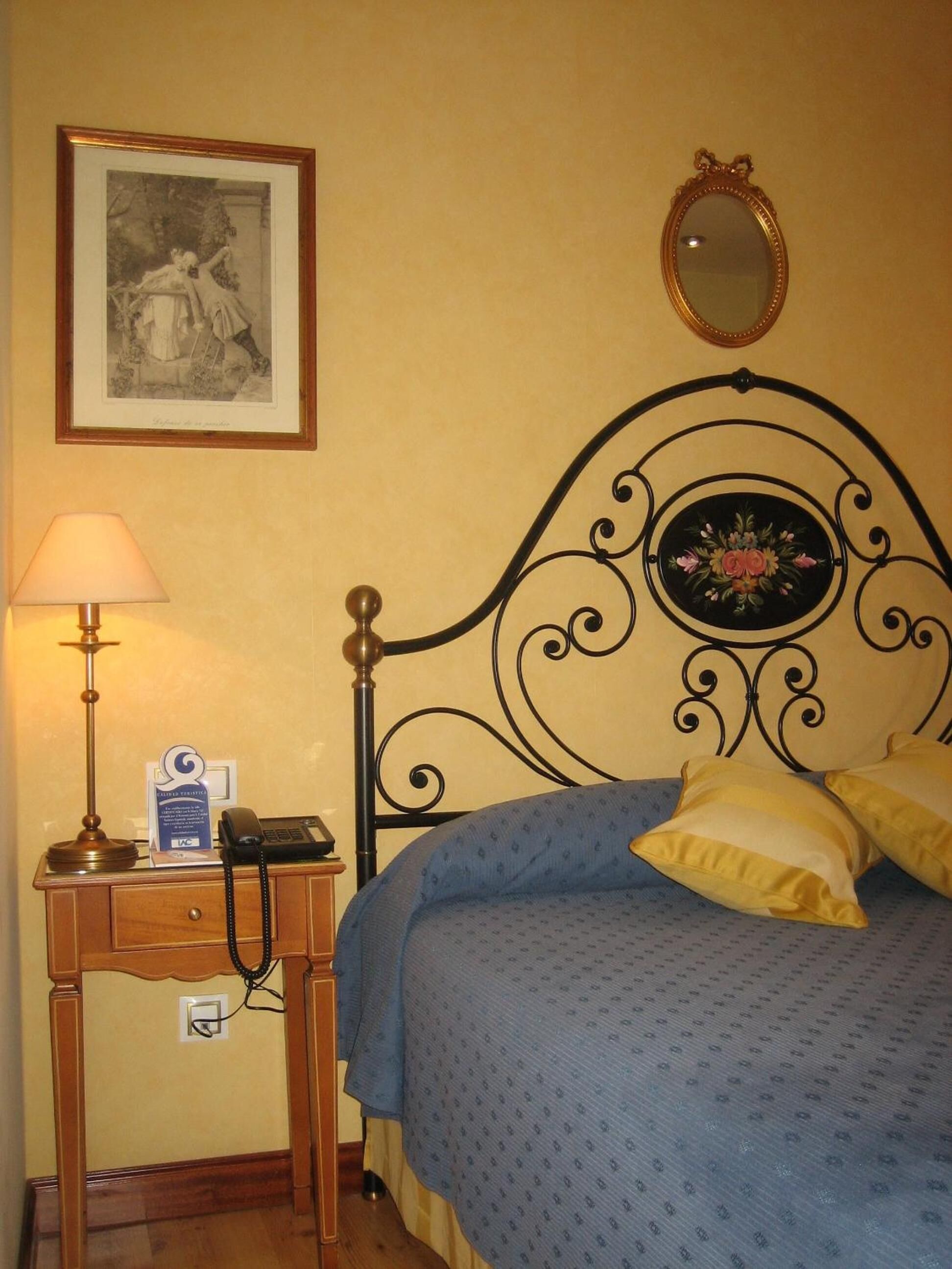 Una habitació d'hotel amb un llit, una taula de nit amb una làmpada, un telèfon i un quadre encimbellat a la paret.