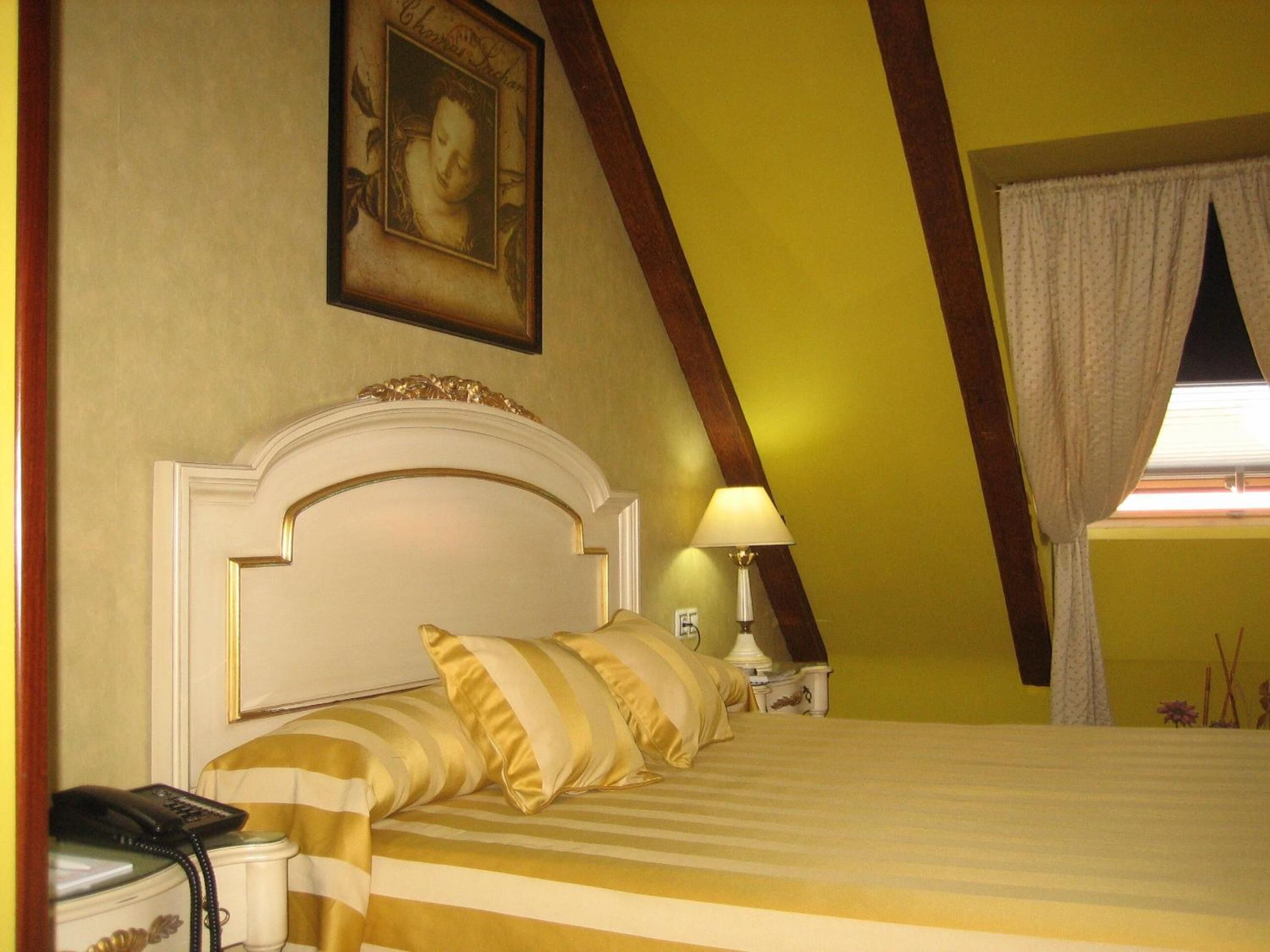 A hotel room with a bed, a nightstand, a lamp, and a painting on the wall.