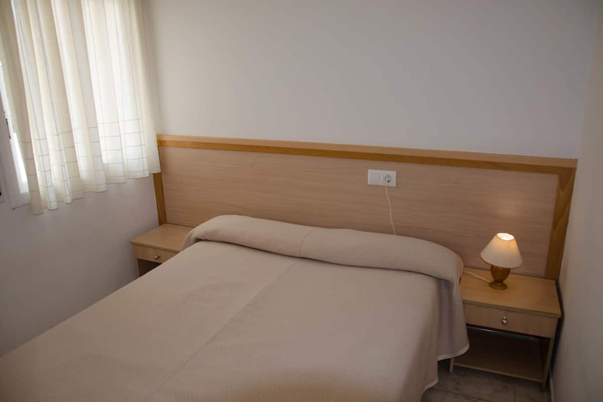 A neatly made bed with a wooden headboard, a bedside lamp, and a nightstand with a drawer.