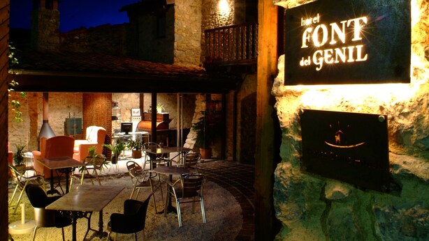 An outdoor seating area with stone walls and a sign for 'Hotel Font del Genil'. - Font Del Genil (Arseguel)