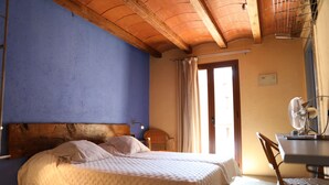 A bedroom with a bed, a chair, a desk, a fan, and a window with curtains. - Font Del Genil (Arseguel)