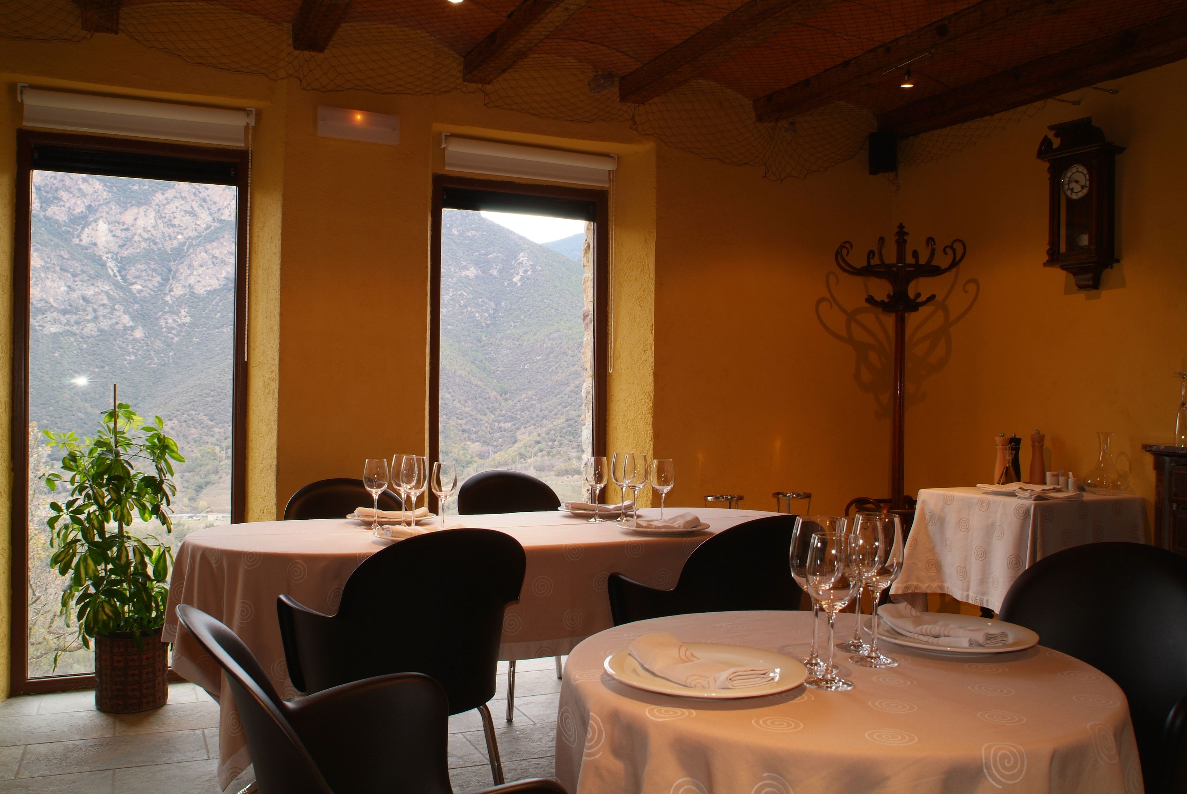 Un comedor con mesas dispuestas para dos, un candelabro y vistas a la montaña a través de amplias ventanas.