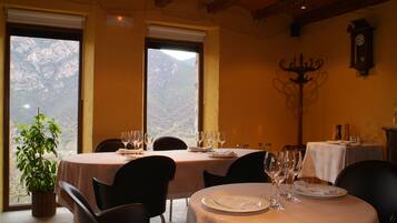 Un comedor con mesas dispuestas para dos, un candelabro y vistas a la montaña a través de amplias ventanas.