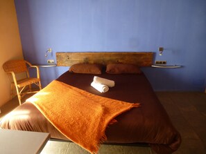 A bed with a wooden headboard, two pillows, a rolled towel, and an orange blanket. - Font Del Genil (Arseguel)