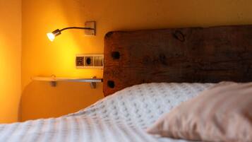 A bed with a white textured blanket and a single pillow, a wooden headboard, and a wall-mounted light fixture.