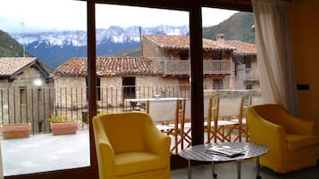 Un balcon avec des chaises jaunes et une table, d’où l’on peut admirer un paysage montagneux parsemé de bâtiments traditionnels.