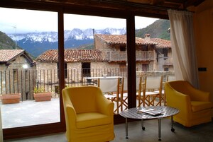 Un balcón con sillas amarillas y una mesa, con vistas a un paisaje montañoso y edificios tradicionales.