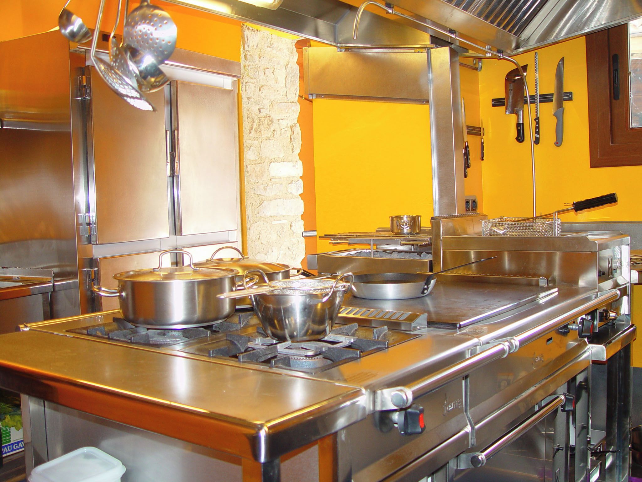 Une cuisine professionnelle équipée d’appareils en acier inoxydable, avec des casseroles sur la cuisinière et divers ustensiles de cuisine.