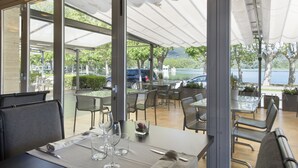 Un espace extérieur aménagé pour les repas, avec des tables et des chaises, de grandes fenêtres et une vue sur le paysage environnant.