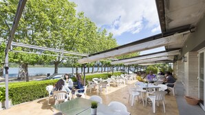 Un espace extérieur aménagé en terrasse, avec des tables et des chaises, offrant une vue sur une étendue d’eau et des arbres.