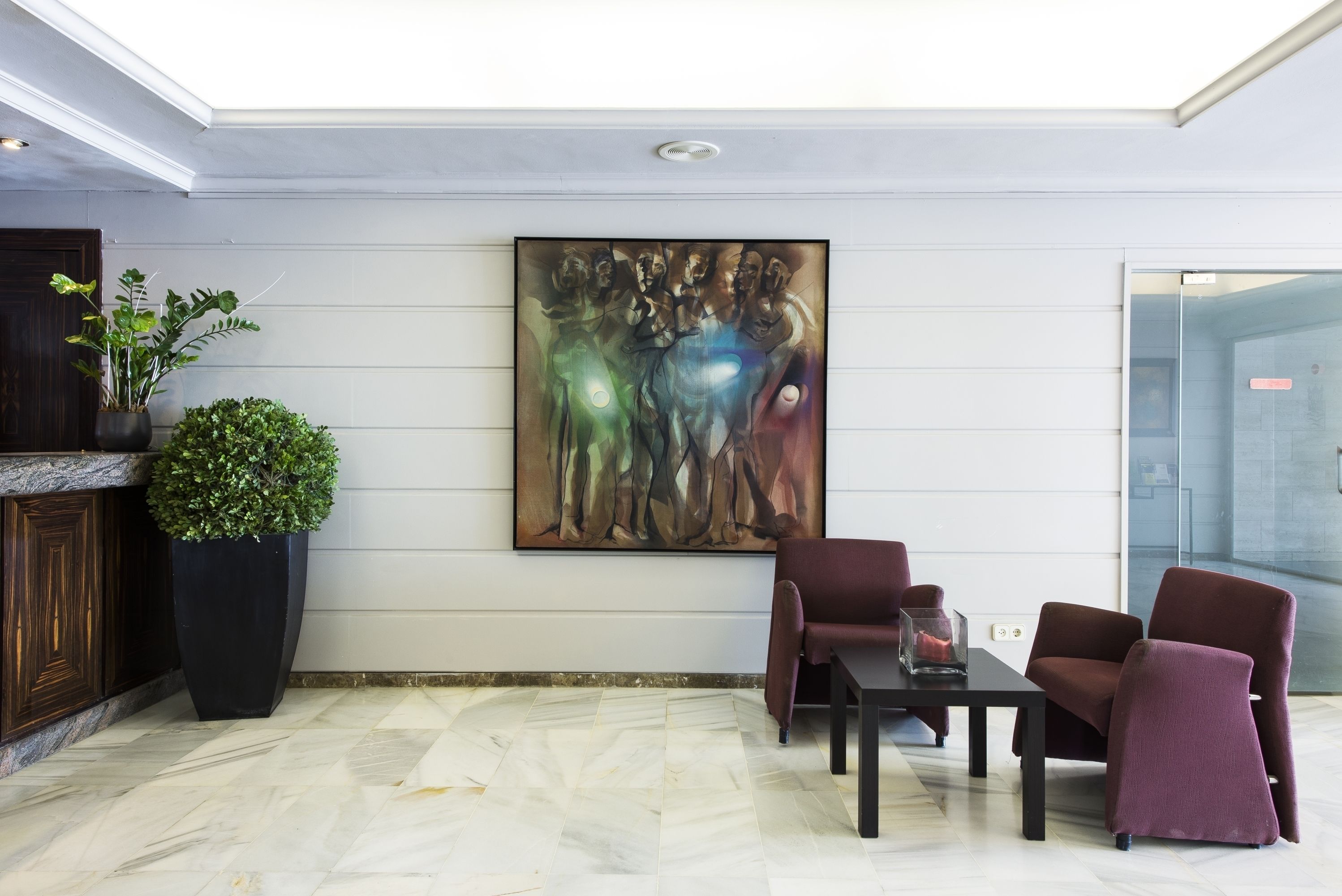 Un hall d’entrée moderne avec un sol en marbre, une grande peinture abstraite, une plante en pot et des sièges aux couleurs sombres.