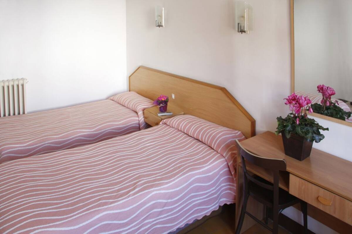 A bedroom with two beds, a wooden desk, and a potted plant.
